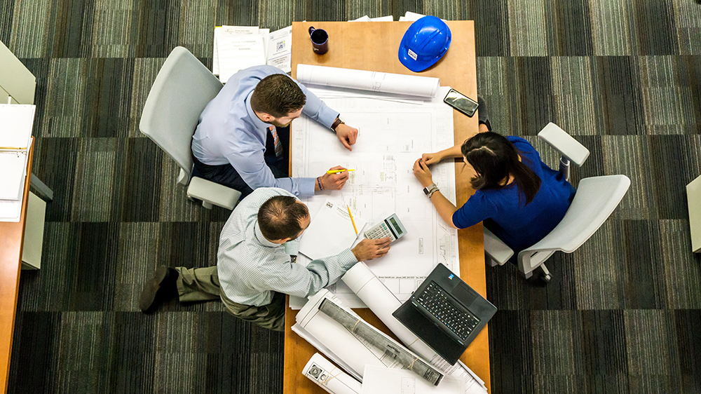 Three people on a table working with construction plans