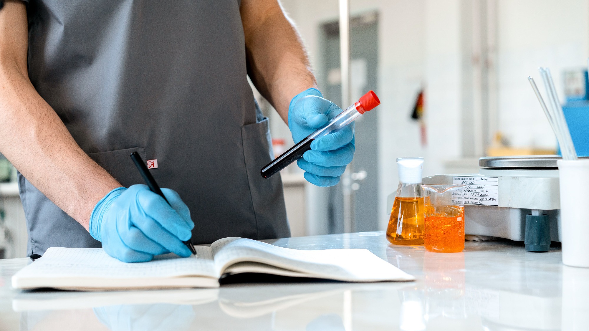 A man writes in a lab notebook and holds a test tube in his hands.
